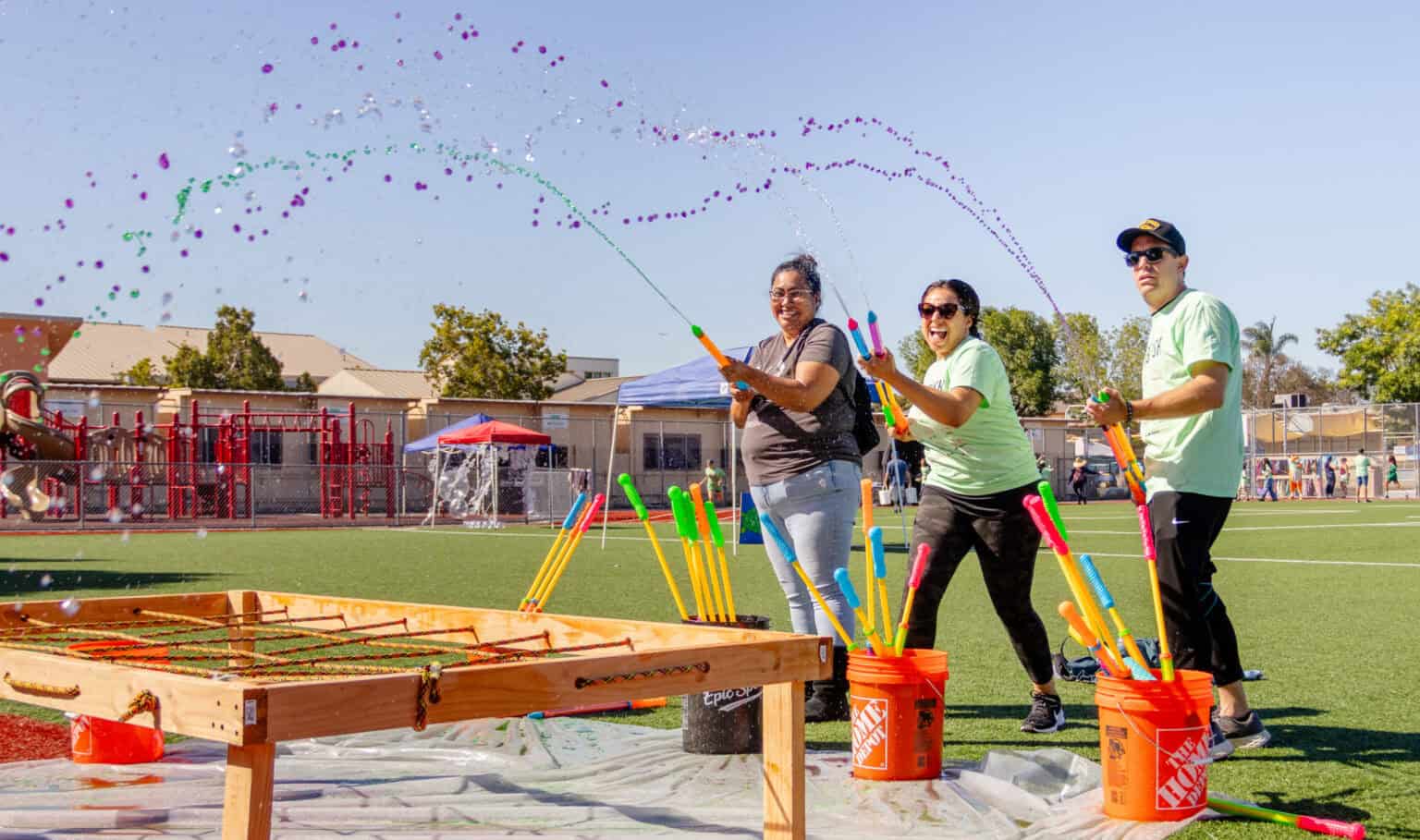 Parents volunteering at jog-a-thon get ready to squirt colored water at runner.