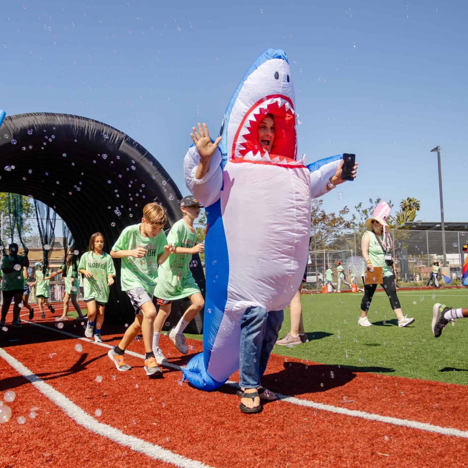 Students run around the track behind a parent wearing a shark costume.