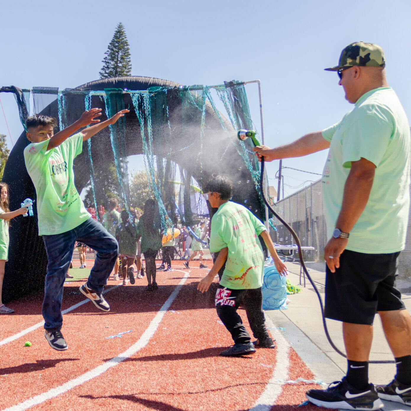 a boy jumps in the air while being sprayed by a hose during the jog-a-thon run.