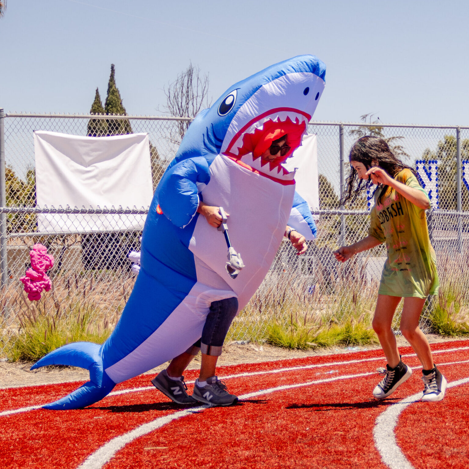 A parent in a shark costume chases a student on the track