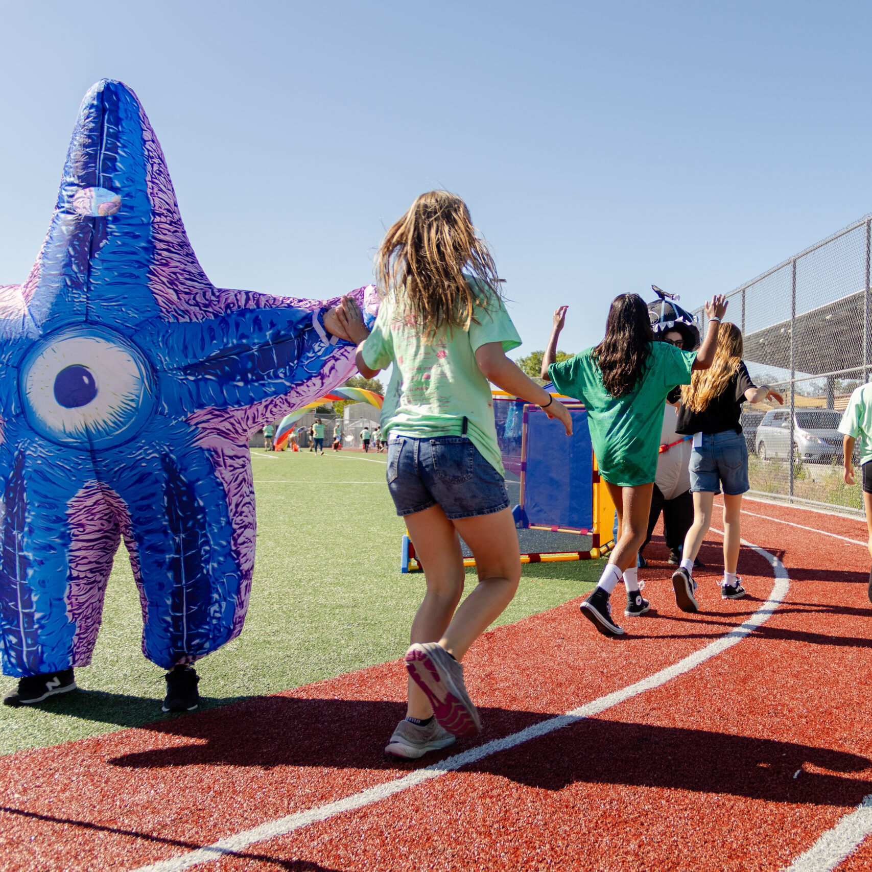 Students high-five a parent in a starfish costume while running around the track.