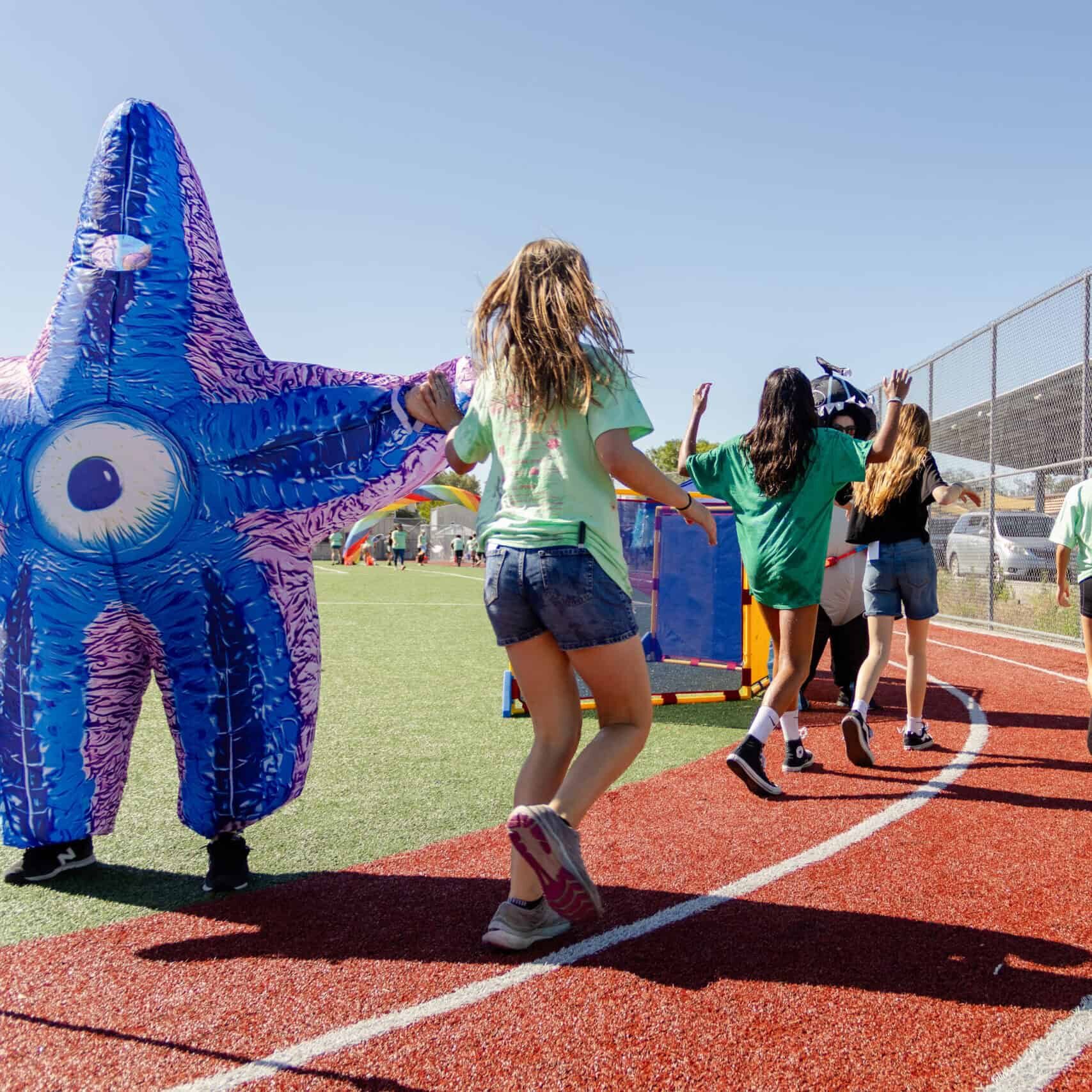 Students high-five a parent in a starfish costume while running around the track.