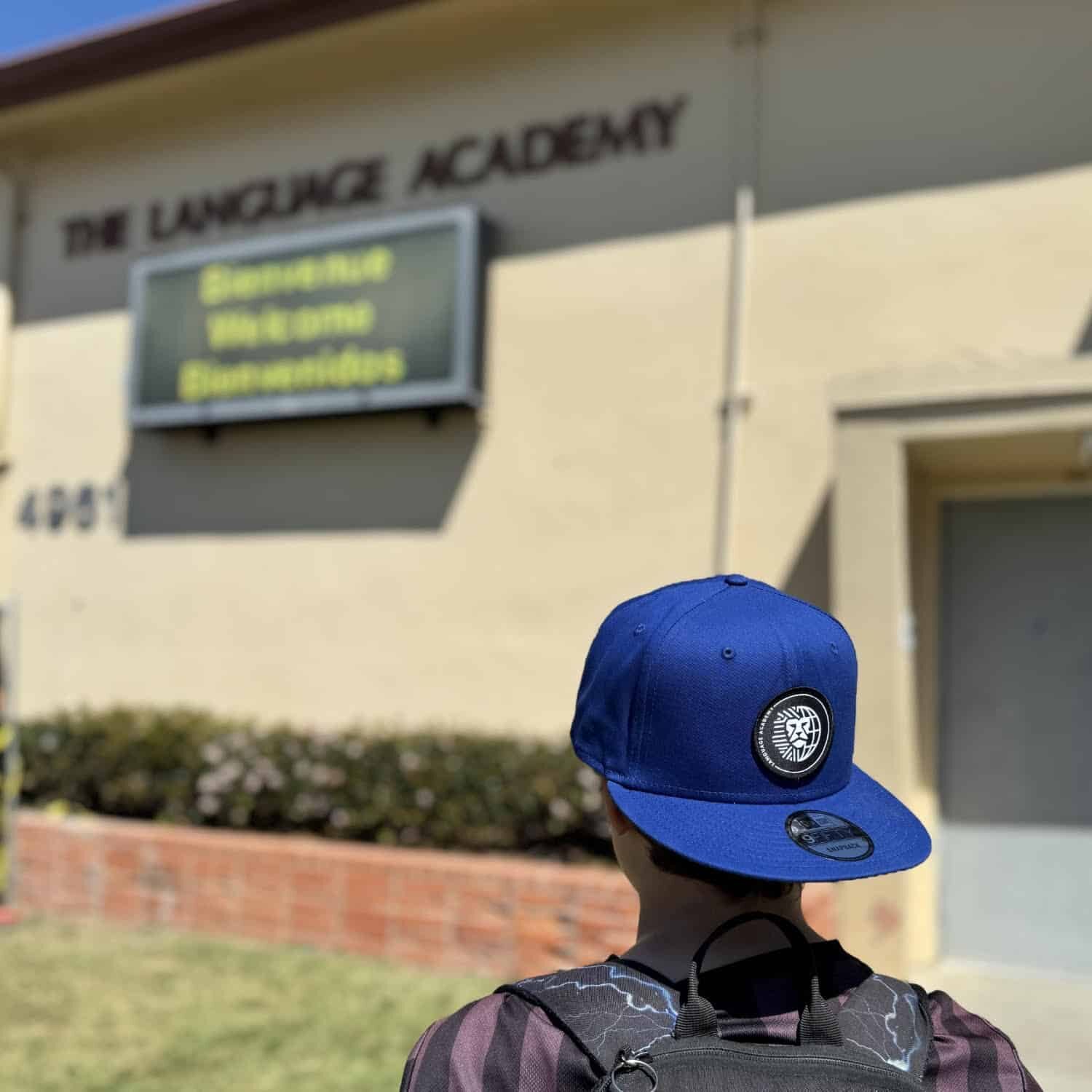 A student wears a backwards hat featuring the new language academy logo in front of the school.
